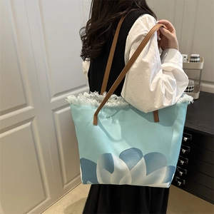 Large blue canvas tote bag with floral print and fringe detail worn by a model