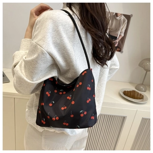 Gros plan d'un sac à bandoulière noir avec imprimé cerises porté par un mannequin