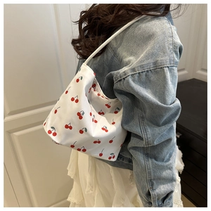 Grand sac à bandoulière en toile avec motif cerises porté par un mannequin en jean