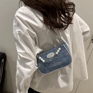 Blue denim baguette bag with pearl chain and metal flower charms worn by a model