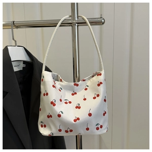 Détail du sac bandoulière blanc avec imprimé cerise et fines anses sur un support