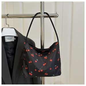 Détail d'un sac cabas noir avec motif cerise et fines bretelles de transport