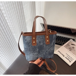 Detail of denim bucket bag with brown leather trim and studs on a minimalist desk