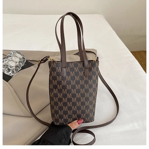 Detailed shot of brown tote bag with M-pattern print on white bedding with a blazer