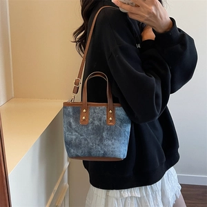 Blue denim crossbody tote bag with brown leather trim and golden rivets shown on model