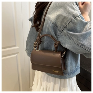Detail of brown crossbody bag featuring knotted handle and gold metal hardware accents