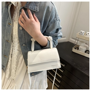 Detail of white leather handbag featuring unique knotted handles and a sleek flap design