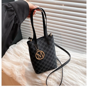 Close-up of black tote bag with repeat M pattern print and golden metal logo charm