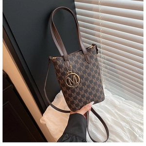 Detail of a brown monogram bucket bag featuring a gold M-pendant and dual handle straps