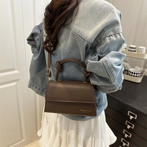 Brown leather handbag with knot handle worn by a model in denim and white skirt