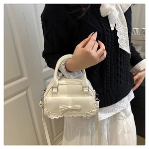 Détail du sac à main crème avec nœud et dentelle sur un fond blanc minimaliste