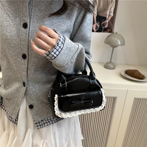 Sac à main chic noir avec dentelle et nœud papillon tenu par un mannequin en intérieur