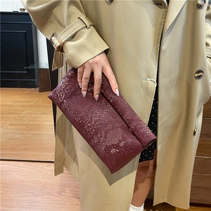 Elegant deep red snakeskin textured clutch bag paired with a classic trench coat style