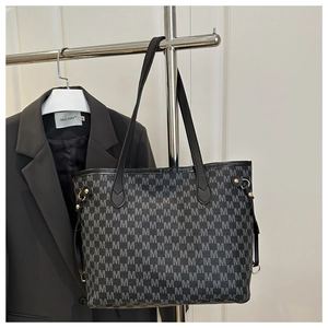 Detail view of black tote bag featuring M-letter monogram pattern and metal zipper closure