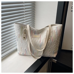 Dettaglio della borsa tote bianca con lettera E a rilievo e ricamo a onde