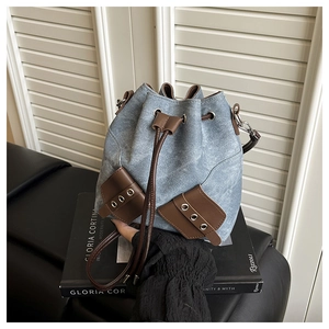 Detail of drawstring bucket bag with light blue denim fabric and brown leather trim