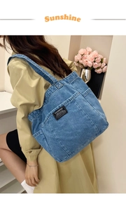 Detail of blue denim tote bag with Fashion Instinct patch worn with a khaki trench coat