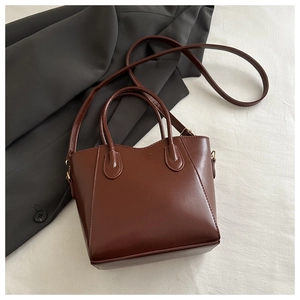 Deep brown bucket bag with dual handles and slim shoulder strap on fabric background