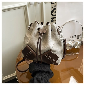 Detail of canvas bucket bag with brown leather trim and metal hardware held by a model