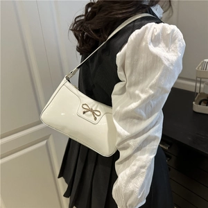 Chic white patent leather underarm bag with gold bow clasp on a model indoors