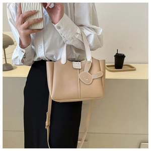 Close-up of beige leather bucket bag featuring a cute rabbit charm and fashion logo