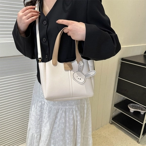 Fashionable beige crossbody bag with brown handles and rabbit charm for outdoor commute