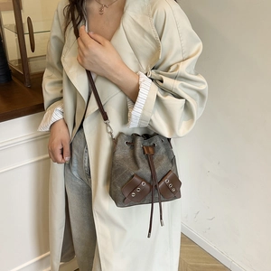 Canvas bucket bag with leather trim and drawstring, worn with a beige trench coat