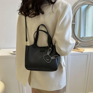 Chic black leather shoulder bag with a cute rabbit pendant shown on a female model