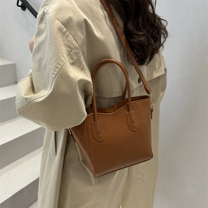 Brown leather tote bag with FASHION embossment carried by a model on white stairs