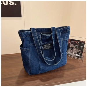 Detail of deep blue denim tote bag featuring side pockets and a branded woven label