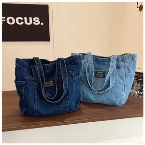 Detail of dark and light blue denim tote bags with side pockets on a wood surface