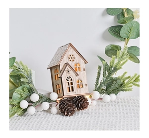 Close-up of wooden Christmas house with LED light, snow-dusted roof and natural pine cones
