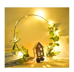 Illuminated Christmas wreath with green leaves, pine cones and small wooden house