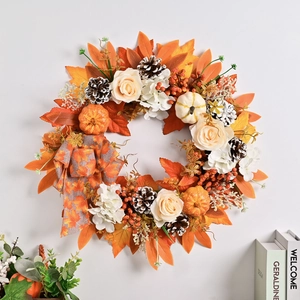 Autumn door wreath with orange maple leaves, pumpkins, and white roses on a white wall