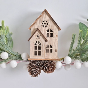Christmas wreath featuring a wooden house, pine needles, white berries and natural pinecones