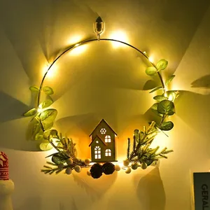 LED Christmas wreath with golden metal ring, eucalyptus leaves, pine cones and wooden house