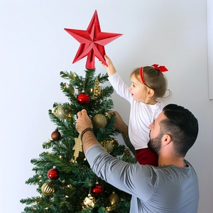 Father and daughter placing a vibrant red metallic star topper on a Christmas tree