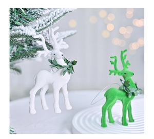 Close-up of white and green flocked reindeer ornaments with holly wreaths on snowy branches