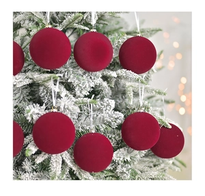 Close-up of deep red velvet Christmas balls hanging on a snowy tree with bokeh lights