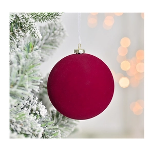 Close-up of deep red velvet Christmas ball with white ribbon on snowy pine tree branch