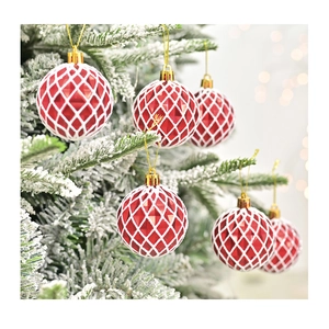 Détail macro d'une boule de Noël rouge avec filet blanc sur une branche de pin enneigée