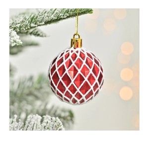 Gros plan d'une boule de Noël rouge à motif losange blanc sur une branche de pin enneigée
