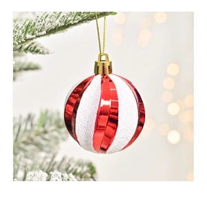 Detail of red and white striped glitter Christmas ball hanging on a snowy tree branch