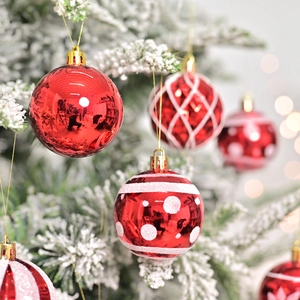 Set de bolas de Navidad rojas con varios estampados colgadas en un árbol de Navidad nevado