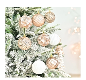 Close-up of rose gold Christmas ball ornaments with geometric patterns on snowy tree