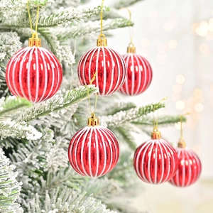 Rood-wit gestreepte kerstbal hangend aan een besneeuwde tak van een kerstboom