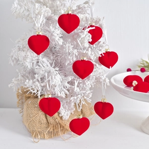 Set of red flocked heart ornaments with gold caps hanging on a white snowy Christmas tree