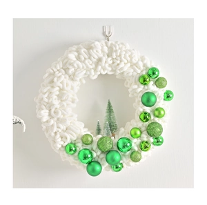 Detail of plush white wreath with green ornaments and mini Christmas trees on white wall