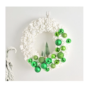 Detail of plush white Christmas wreath with green ornaments and miniature pine trees