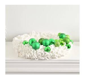 Detail of white chunky knit Christmas wreath with green ornaments on a white mantel